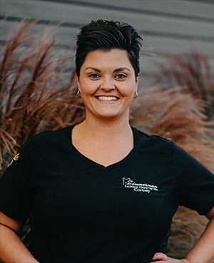 A smiling woman wearing a black shirt with a logo and standing in front of a building.