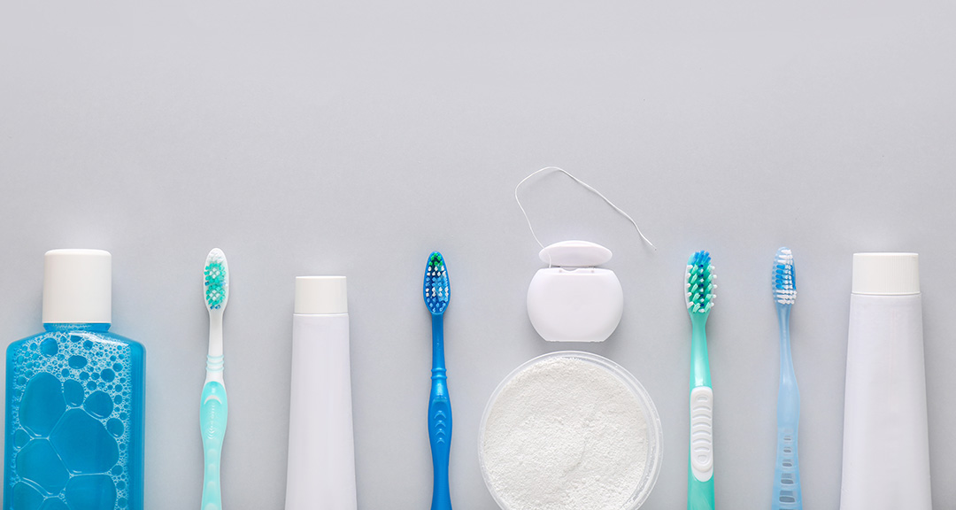 The image displays a collection of various oral hygiene products, including toothbrushes, toothpaste, and mouthwash, against a white background.