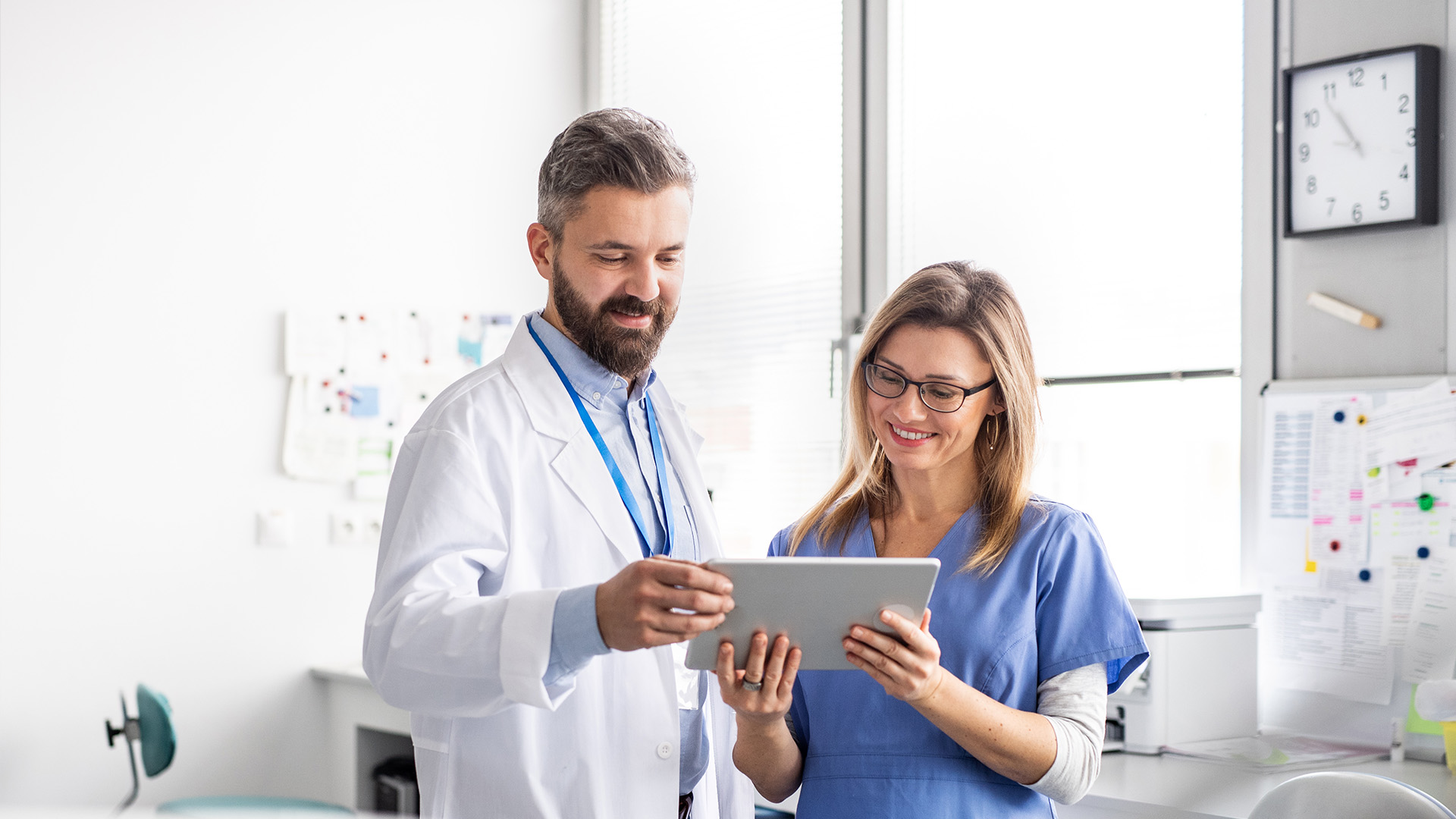 A man and a woman in a medical setting, the man is holding a tablet.