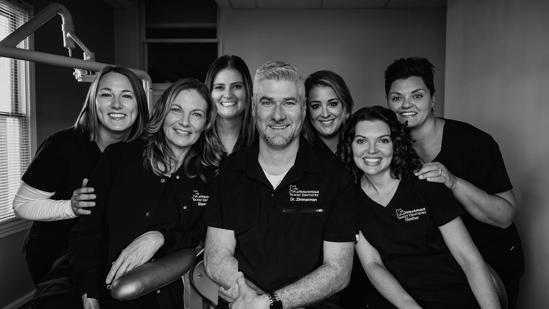 The image features a group of individuals in a dental office setting, posing for a photograph with smiles.