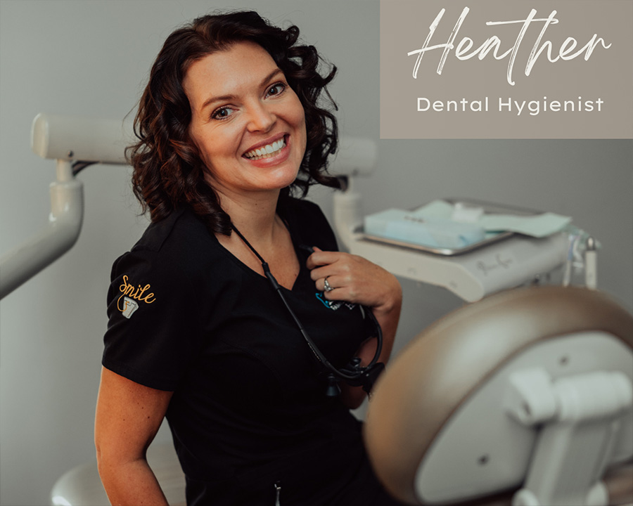 A woman in a dental hygienist uniform, smiling and posing with a dental chair behind her.