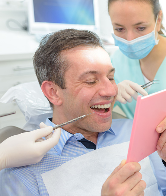 Man in a dental chair, smiling broadly at the camera while holding a pink object with both hands.