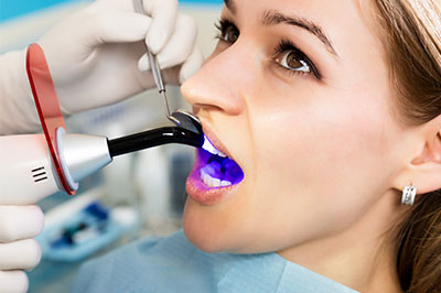 Woman receiving dental treatment, with a dentist using a device to clean or examine her teeth.