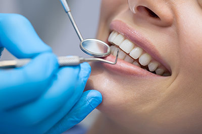 A dental hygienist is performing a teeth cleaning procedure on a patient s mouth, with the focus on the professional s hands using tools and the smiling face of the patient.