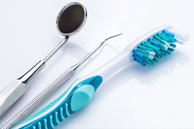 The image shows a collection of dental tools, including a toothbrush and a pair of scissors with blue handles, arranged on a white surface.