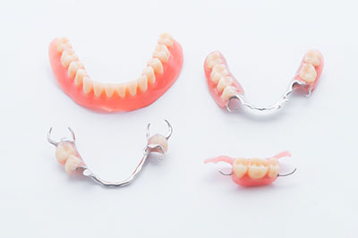 A collection of three dental bridges with artificial teeth, showcasing a set for upper front teeth and two sets for lower front teeth, displayed against a white background.