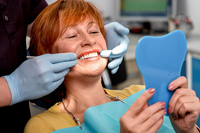 Woman in a dental chair receiving oral care, with a blue model of a mouth held up to her face.