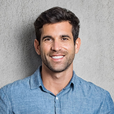 The image shows a man smiling at the camera, with a neutral background and a relaxed pose.