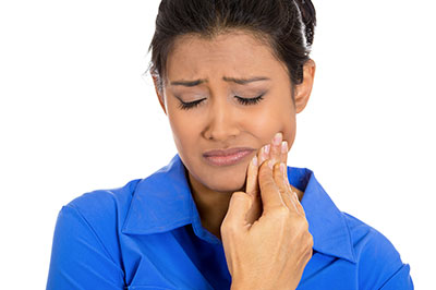 The image features a woman with her hand on her face, looking concerned or distressed. She appears to be in the process of applying something to her nose or mouth area. The background is plain and does not provide any additional context about the setting or situation.