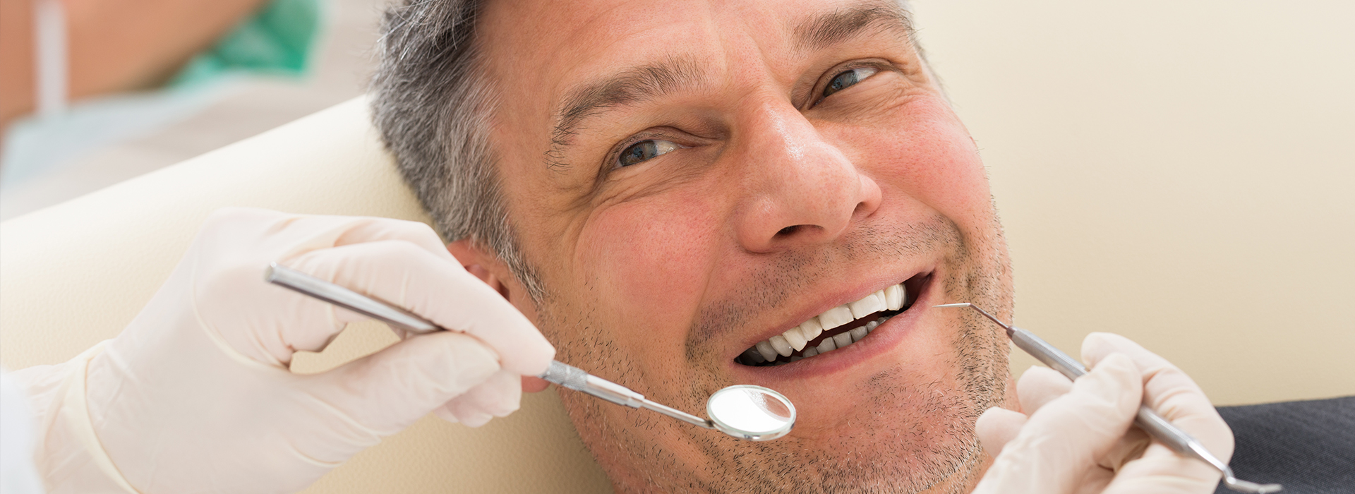 A man in a dental chair receiving treatment, with a smiling expression and a dentist attending to him.