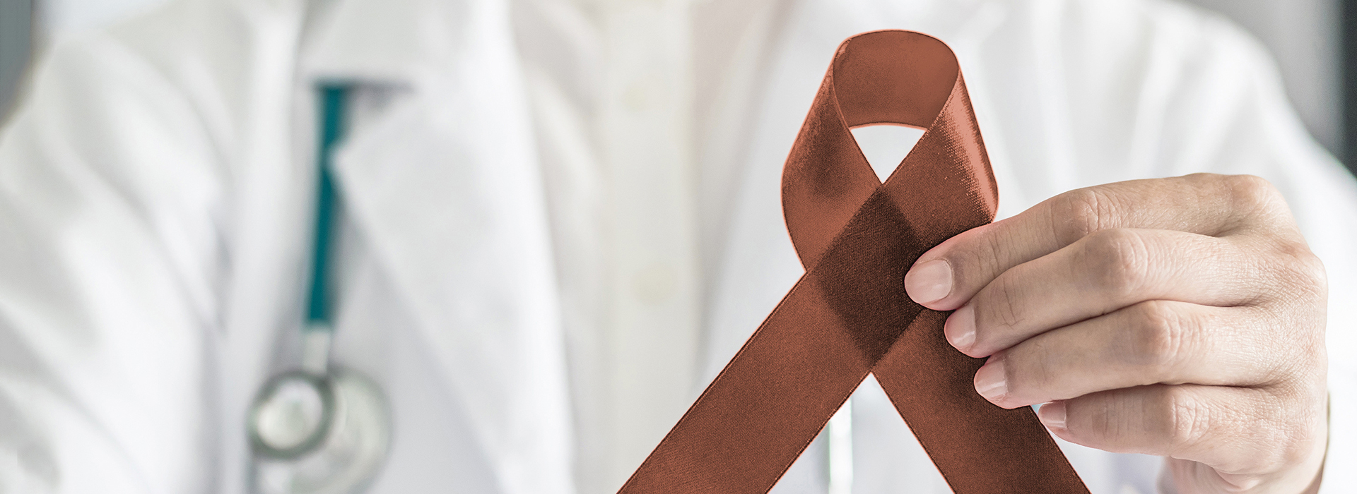 The image shows a healthcare professional holding up a red ribbon with a white symbol on it, which is commonly associated with awareness for cancer.