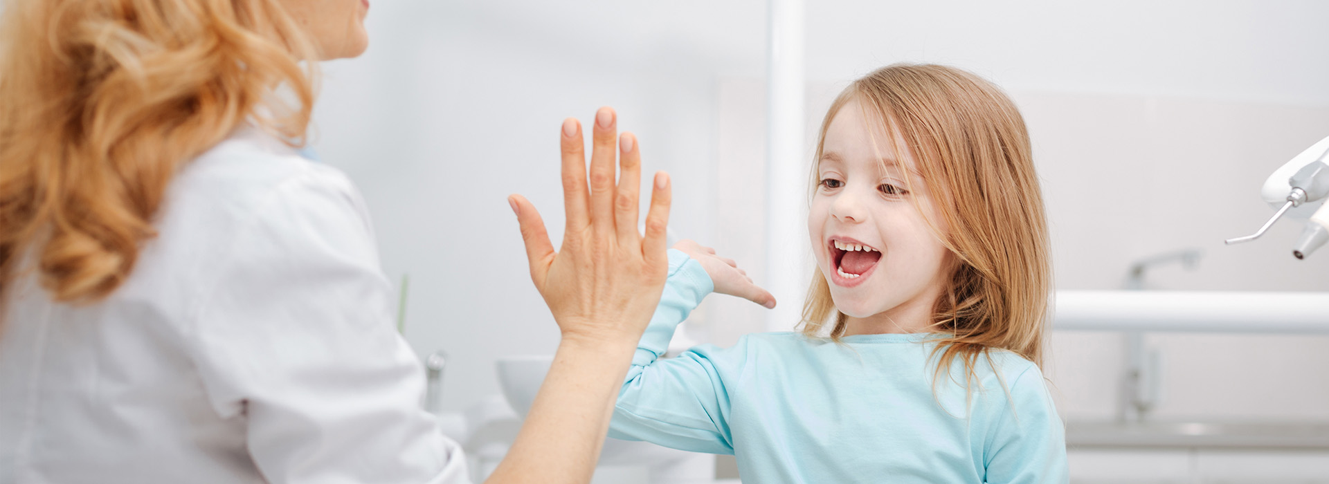 The image shows a woman and a young girl in a dental office, with the woman gesturing towards the child.