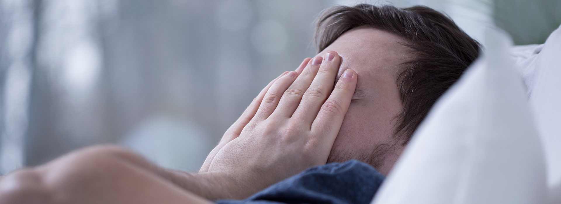 The image shows a person lying in bed, holding their face with both hands, appearing to be distressed or upset.