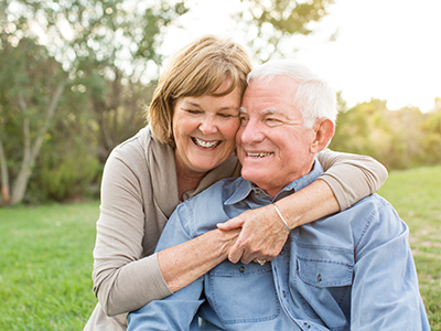 An elderly couple embracing in a park setting with a clear sky.