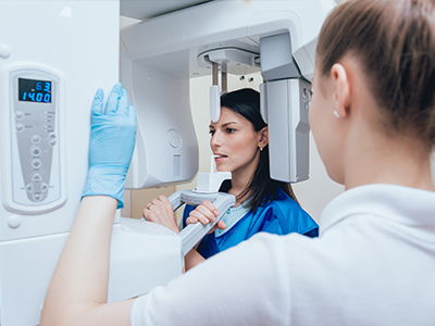 A woman in a blue coat inspecting a large, white medical imaging machine with a smiling technician standing beside it.