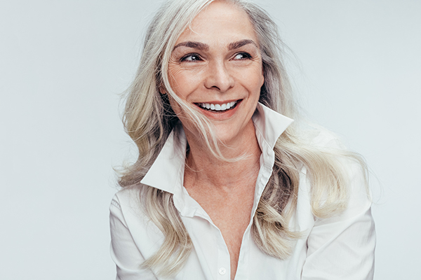 The image shows a woman with short hair, wearing a white shirt, smiling broadly and looking directly at the camera.