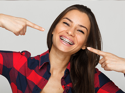 Woman with a playful expression pointing to her teeth, smiling broadly.