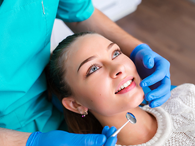 The image depicts a dental professional performing a dental procedure on a patient, with the patient smiling and wearing protective eyewear.