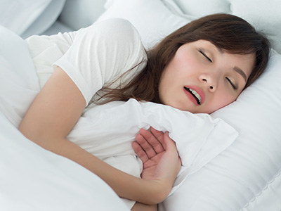 A woman sleeping peacefully with her eyes closed in a bed with white sheets and pillows.