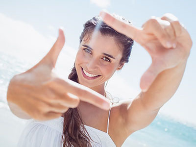 A young woman with long hair is smiling and holding a smartphone up to her face, capturing a selfie.