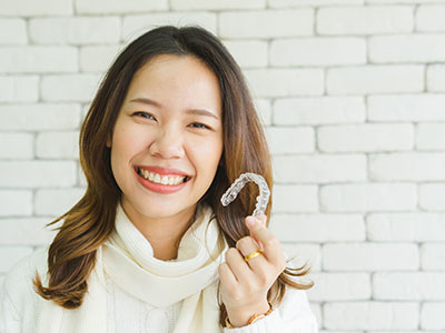 A smiling woman holding a dental appliance in front of her mouth.